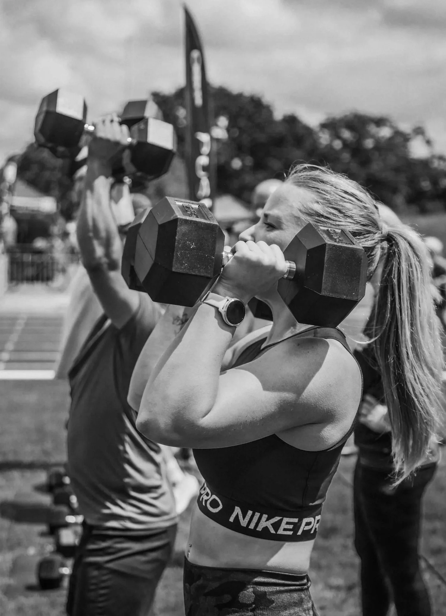 นักกีฬากำลังยกดัมเบลสองอันขึ้นเหนือหัวในท่า Push Press Labour